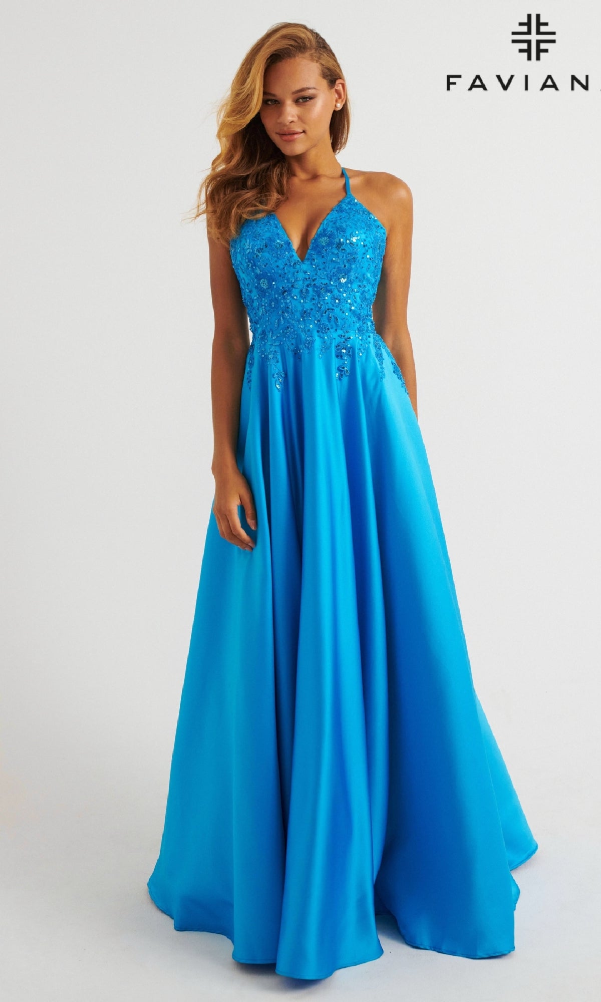 A woman in the Faviana 11260 Long Prom Dress—sleeveless, bright blue satin with a lace embroidered bodice and flared skirt—stands before a plain white background featuring the Faviana logo.